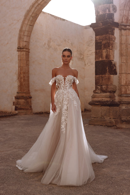 Suknia ślubna Ariella od DAMA Couture ma gorset z przezroczystymi fiszbinami i bogatymi, kwiatowymi aplikacjami koronkowymi tworząc efekt eterycznej elegancji.