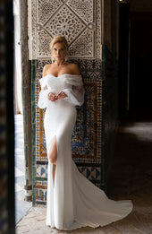 Gładka suknia ślubna w stylu syrenki z opadającymi na ramiona  długimi rękawami oraz spódnicą z rozporkiem i trenem z pracowni sukien ślubnych Dama Couture (zdjęcie główne)