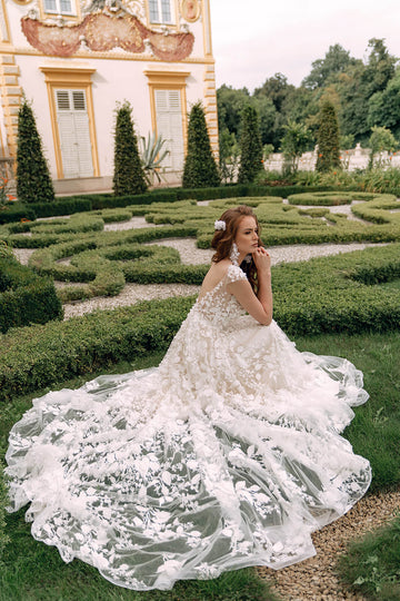 Modna suknia ślubna w stylu księżniczki z krótkim rękawem i finezyjnym dołem, cała wykończona kwiatową koronką 3D z trenem z pracowni sukien ślubnych Dama Couture (zdjęcie bok)