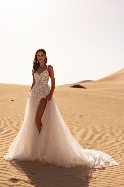 The Aviva bridal gown with a long tulle train and soft veil exudes ethereal elegance in the desert landscape.