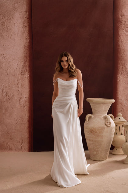 Elegancka suknia ślubna Eleonore o dopasowanym kroju z odkrytymi ramionami i perłowymi ramiączkami zachwyca subtelną klasyką i ponadczasowym wdziękiem.