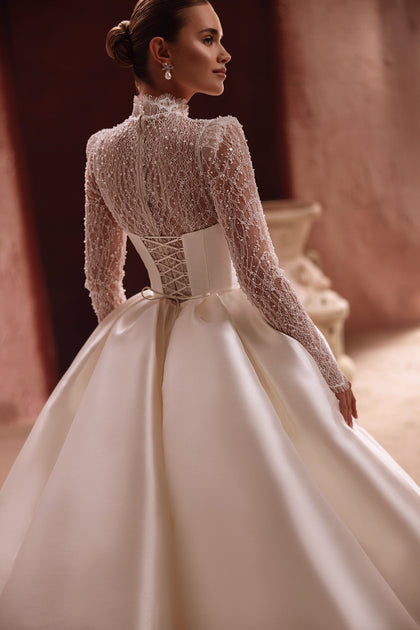 The Henriette wedding dress combines a beaded lace bodice with a detachable satin overskirt for a regal and versatile bridal look.