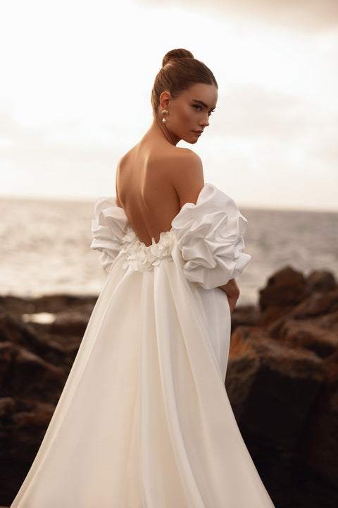 Suknia ślubna z odkrytymi plecami i bufkami ozdobionymi kwiatowymi detalami, nadająca stylu haute couture.