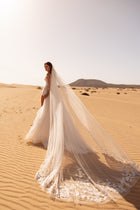 Welon Aviva to długi welon ślubny z tiulu w stylu cathedral z subtelnymi koronkowymi zdobieniami na dole, idealny do romantycznej sesji w plenerze.