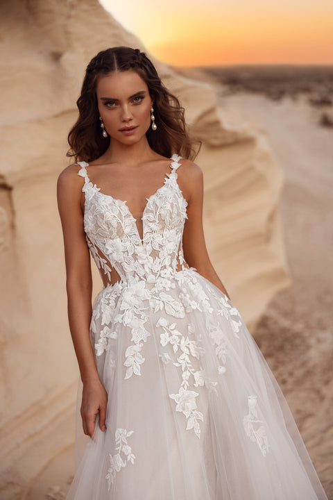 The Zafira wedding dress with a tulle skirt and floral lace details, paired with a groom in a beige suit, creates a dreamy bridal look.